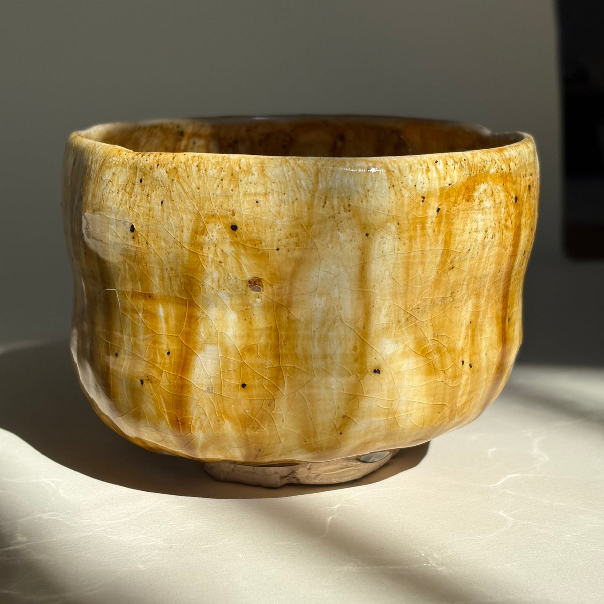 A hand carved ceramic bowl with a textured, organic shape, made using the Kirunuki technique. Featuring a marbled glaze of ochre yellow, cream, and brown. 